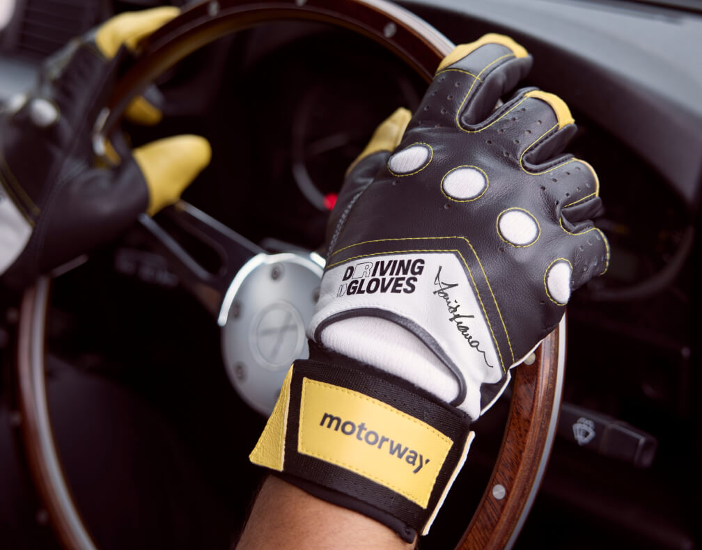 A pair of hands sporting the signed David Seaman Driving Gloves, resting upon the wheel of a vintage car
